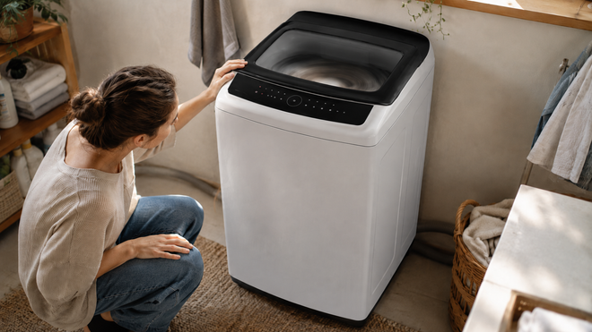 A person checking a white top-load washing machine shaking during the spin cycle in a home laundry room.