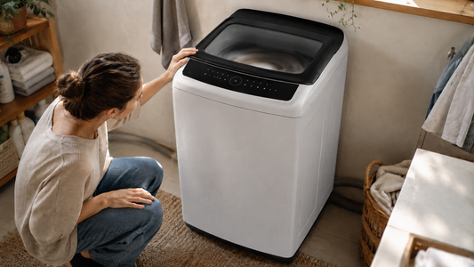 A person checking a white top-load washing machine shaking during the spin cycle in a home laundry room.