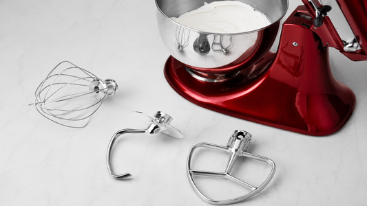 KitchenAid tilt-head stand mixer beside a flat beater, dough hook, and wire whip